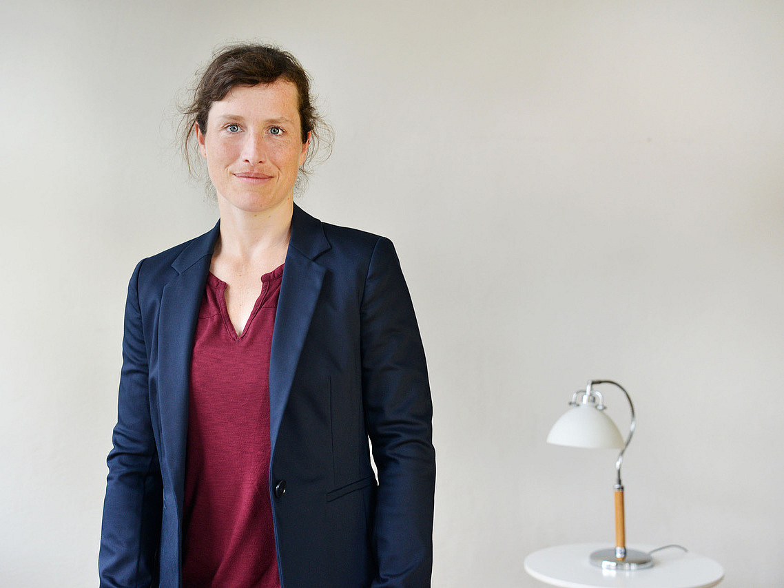 Frau im blauen Blazer neben Tisch mit Lampe