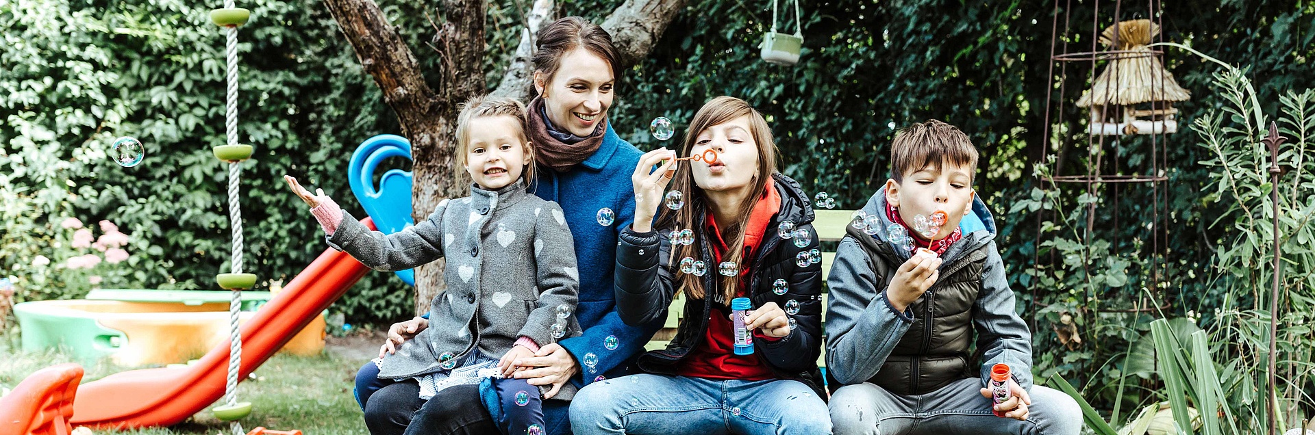 Familie sitzt auf Bank im Garten und macht Seifenblasen