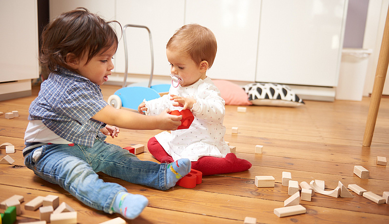 Kleinkind und Baby sitzen auf dem Fußboden und spielen mit Bausteinen