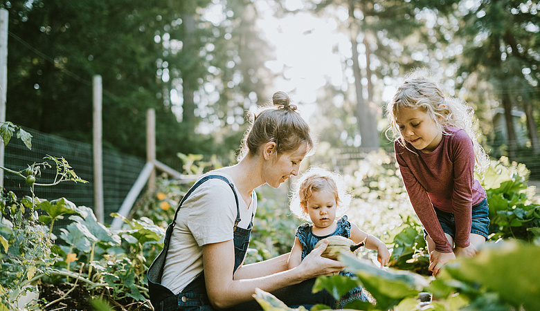 Frau sitzt mit ihren beiden Kindern, zwei Mädchen, und erntet Zucchini