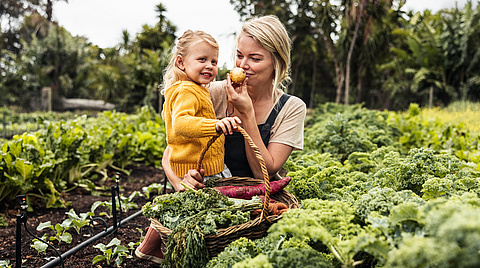 Frau mit Kind auf dem Arm in einem Gemüsefeld