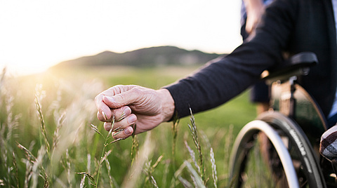 Rollstuhl auf grüner Wiese, Hand fährt durchs Gras