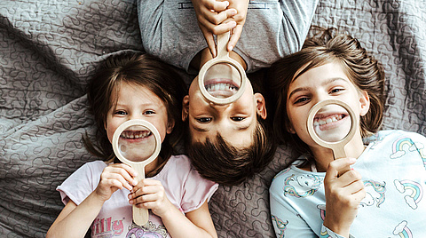 Drei Kinder halten Lupe vor Ihre Zähnen