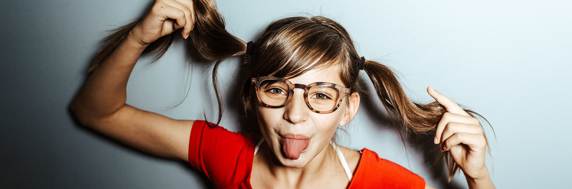 Kleines grinsendes Mädchen mit Zöpfen und Brille 