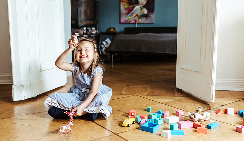 Kind sitzt auf dem Fußboden mit vielen Bausteinen und lacht