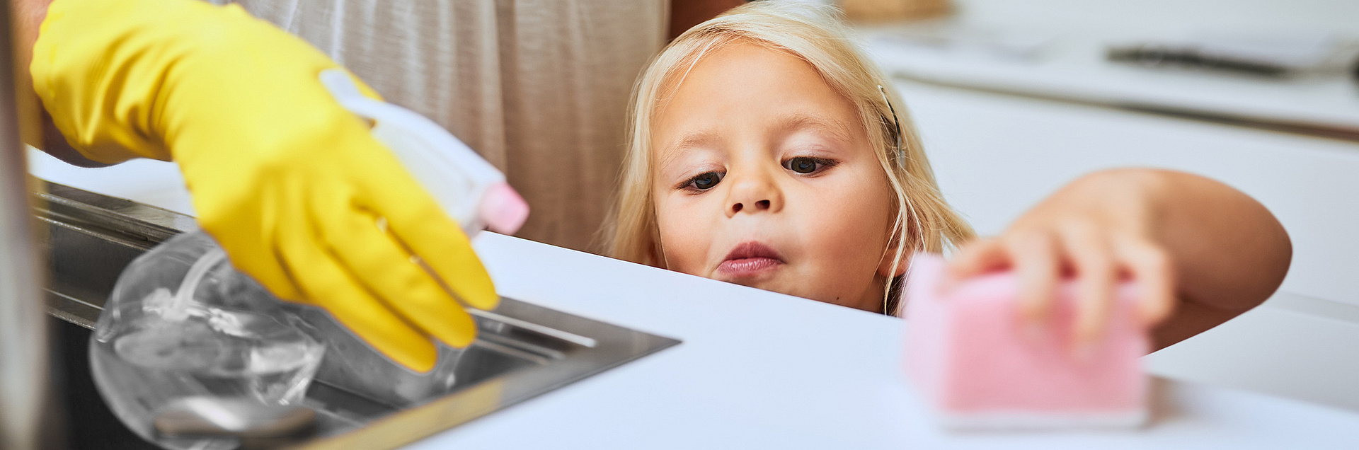 Kind wischt mit einem Schwamm den Tisch ab, Frau ist behilflich