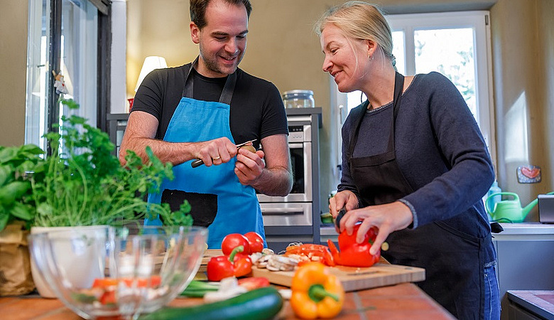 Ein Mann und eine Frau beim Gemüseschneiden, unter anderem Gurke, Tomaten und Paprika