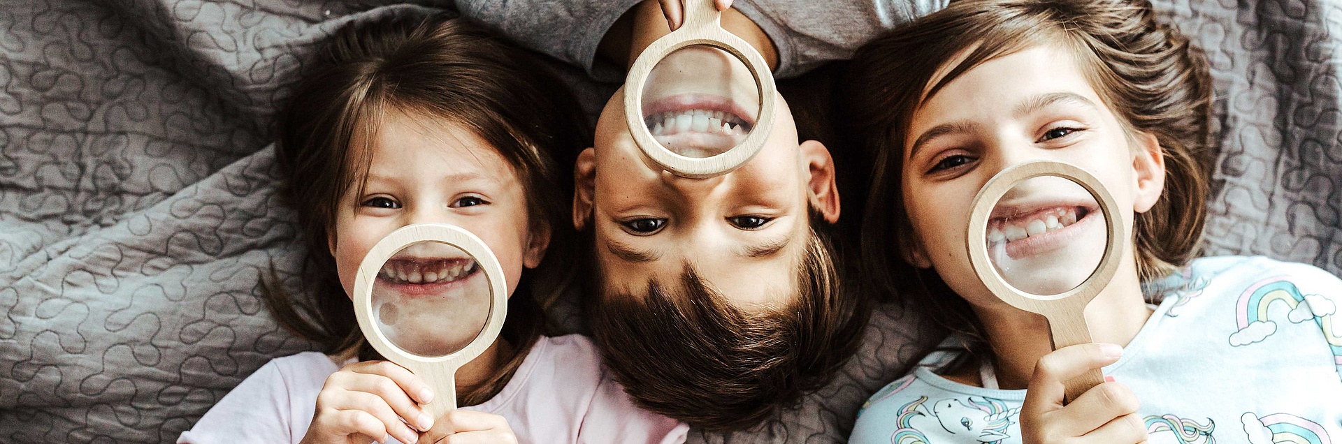 Drei Kinder halten Lupe vor Ihre Zähnen